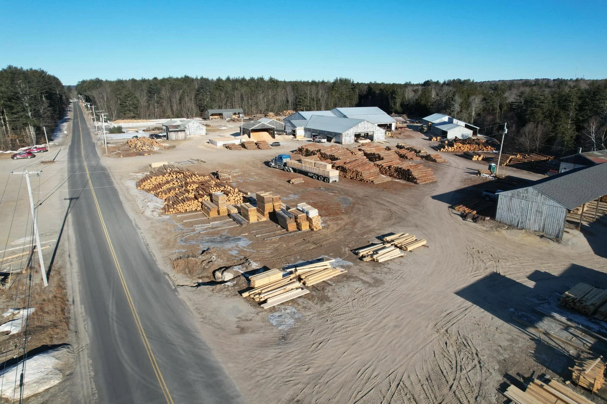 Aerial view of the Maschino & Sons Lumber yard, with log piles, stacked lumber and mill buildings along Morse Rd